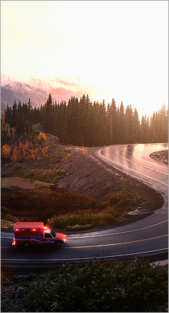 An ambulance is driving on a road in the mountains, trees in the background.